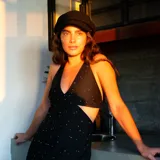 Vestido corto negro con estampado de hojas doradas, escote en V, breteles finos cruzados en la espalda, cut-outs laterales bajo el busto y volado en el ruedo.