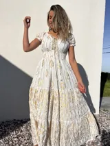 Vestido largo blanco con estampado dorado, escote en V con cordones y mangas cortas abullonadas.