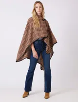 Ruana tejida de la marca Jones New York, con estampado a cuadros en tonos marrón, beige y blanco. Presenta cuello alto y cierre frontal con botón trenca y botón a presión interno. Los bordes están ribeteados en negro.