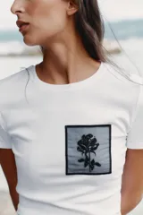 Camiseta blanca de algodón con cuello redondo y mangas cortas. Presenta un bolsillo de tul con una flor bordada y abalorios en el delantero.