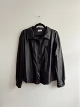 Sobrecamisa oversize de ecocuero color negro, con bolsillo delantero y puños ajustables.