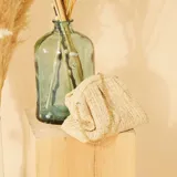 Bolso bandolera color beige, tejido en rafia con patrón de espiga. Tiene forma rectangular con cierre superior fruncido y cadena dorada para colgar al hombro.