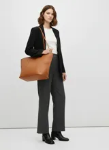 Bolso shopper de efecto cuero color coñac, de gran tamaño, con asas cortas para llevar en mano y correa ajustable para llevar al hombro. Presenta un diseño liso con costuras verticales marcadas en el frente.