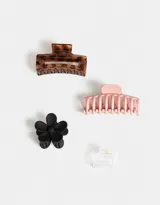 Set de cuatro broches para el pelo de diferentes formas: dos broches rectangulares, uno con diseño carey y otro rosa pastel; un broche con forma de flor negro; y un broche rectangular transparente.