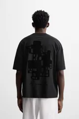 Camiseta negra de corte holgado, cuello redondo y manga corta. Estampado frontal con texto vertical y diseño geométrico abstracto en negro.