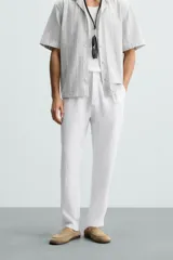 Pantalón de vestir blanco, confeccionado en lino, de corte recto, con bolsillos laterales y traseros. Se ajusta a la cintura con botón y cierre.