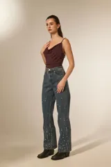 Pantalón jean color natural de calce alto y corte recto, con bolsillos y detalles de strass dispersos por las piernas.