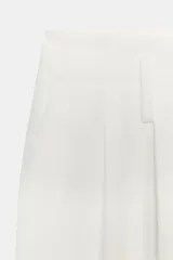 Pantalón marrón de tiro alto con bolsillos delanteros y falsos bolsillos traseros con tapeta. Detalle de pliegues en la parte delantera. Cierre frontal con cremallera y gancho metálico.