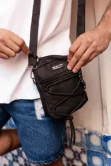 Morral bandolera negro de poliéster con correa ajustable, cierre superior y bolsillo frontal con red elástica.