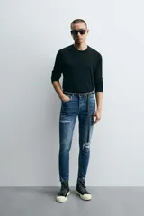 Pantalón de jean azul oscuro con efecto lavado y roturas en las rodillas, de corte ajustado al cuerpo desde la cintura hasta el tobillo.