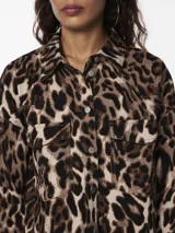 Camisa animal print con estampado de leopardo en tonos marrones y beige. Tiene cuello camisero, mangas largas con puños abotonados, cierre frontal con botones y dos bolsillos de parche en el pecho.