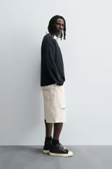 Polo negro de corte relaxed fit confeccionado en tejido con algodón. Cuello solapa con cierre frontal de botonadura. Manga larga. Bajo con aberturas laterales. Acabados en rib.