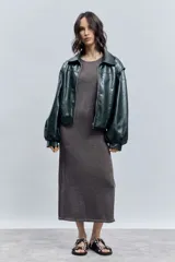 Cazadora corta de efecto piel color verde oscuro, con cuello solapa, cierre frontal de cremallera y mangas largas abullonadas con puños elásticos.