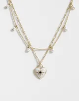 Collar corto dorado con doble cadena, una con eslabones y otra con perlas colgantes. Dije de corazón con strass incrustado.