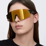 Lentes de sol Meller Dua con montura negra y lentes doradas reflectantes. Diseño deportivo inspirado en el ciclismo, con estructura sin montura y forma de pantalla. Protección UV400 - Categoría 3.