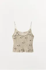 Top de crochet color beige, con tirantes finos y escote redondo. Presenta apliques de flores en relieve y abalorios plateados.