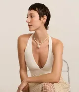 Collar corto con cordón torcido color crema y colgante grande de caracola con detalles dorados.