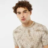Remera beige con estampado de hojas de palmera en tonos marrones.