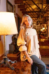 Blusa color beige de algodón, con cuello alto con volado, mangas largas abullonadas con elástico en los puños y detalle de botones forrados en la espalda.