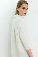 Vestido corto de denim color blanco, con cuello camisero, mangas cortas, dos bolsillos frontales y ajuste con cordones cruzados en el escote.