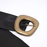 Cinturón ancho de color negro con hebilla cuadrada dorada y múltiples ojales metálicos.