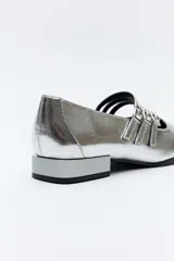 Zapato tipo Mary Jane color negro con textura de reptil, de charol sintético con punta cuadrada y triple tira con hebillas.