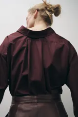 Camisa color borgoña de Zara Woman Collection, confeccionada en algodón popelín. Tiene cuello solapa, escote en pico, mangas largas con puños abotonados, bajo redondeado y cierre frontal con botones.