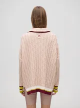 Sweater tejido de algodón color rosa claro, con cuello polo con cierre de cremallera metálica y mangas largas con puños a rayas de colores.