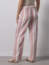Pantalón de lino color blanco con rayas verticales rosas y celestes. Tiene pretina ancha elastizada con lazo de ajuste y bolsillos inclinados en la parte delantera.