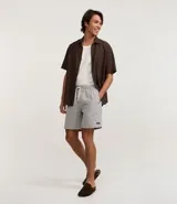 Bermuda de sarga con estampa rayada en color gris, de corte recto y largo por encima de la rodilla. Posee cintura elástica ajustable mediante cordón blanco y bolsillos laterales.