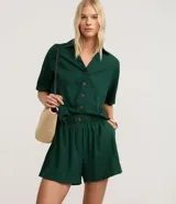 Short blanco de corte runner evasé, con cintura elástica fruncida y un botón decorativo. Presenta bolsillos laterales y un calce suelto.