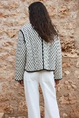 Campera corta acolchada de algodón con estampado floral en blanco y negro, cuello redondo, cierre frontal con botones a presión, bolsillos delanteros de parche y forro de algodón.