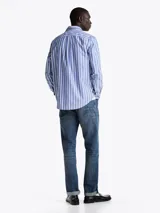 Camisa de popelín de algodón a rayas verticales azules y blancas, de corte regular, con cuello abotonado, puños redondeados con botón y logo de Tommy Hilfiger bordado en el pecho.