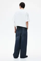 Pantalón de jean azul oscuro de corte holgado, con tiro bajo, cinco bolsillos y pierna extra ancha con pliegues en el tobillo.