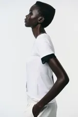 Camiseta blanca de algodón con cuello redondo y mangas cortas con detalle de encaje negro.