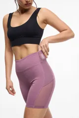 Calza deportiva corta color lila, de cintura alta, con bolsillos laterales y transparencias de microtul en los laterales.
