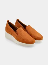 Mocasín slip-on de mujer color coñac (marrón anaranjado) con capellada de gamuza perforada y suela plataforma blanca gruesa y curva.