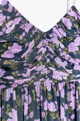 Vestido largo negro con estampado floral en tonos lila y verde. Escote en pico, tirantes finos, detalle drapeado en el busto, forro interior y cierre lateral con cremallera oculta.