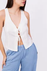 Chaleco corto sin mangas color verde salvia, confeccionado en tela perforada (broderie o calado). Presenta escote en V con lazos ajustables en el centro frontal.