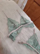 Conjunto de lencería de encaje floral color verde menta, con detalles y tiras ajustables en tono beige/tostado. Incluye un corpiño triangular sin aro y una bombacha tipo colaless o tanga.