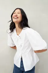 Blusa blanca de algodón con mangas abullonadas, escote redondo y lazos frontales.