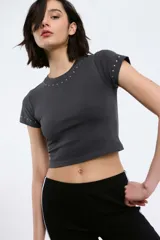 Remera gris oscura de corte crop, con cuello redondo y mangas cortas. Presenta tachas plateadas alrededor del cuello y en las mangas.