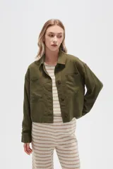 Chaqueta color blanco hueso de lino con cuello camisero, cierre frontal con botones marrones, bolsillos de parche en el pecho y corte holgado.