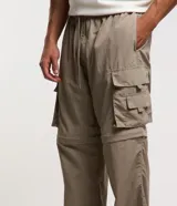 Pantalón paper touch color verde militar, con bolsillos laterales, cintura elástica y cordón de ajuste. Se convierte en bermuda gracias a un cierre a la altura de la rodilla.