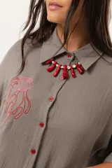 Camisa verde de silueta oversize con cuello camisero y manga 3/4. Tiene bordados de coral y caracol en el frente y botones a tono.