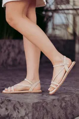 Sandalias chatitas color beige con tiras cruzadas y pulsera al tobillo, decoradas con tachas doradas.