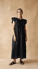 Vestido midi negro de lino 100% con volados en los hombros y dos bolsillos delanteros grandes. Presenta pespuntes contrastantes en color beige que resaltan el cuello, los bolsillos y el ruedo.