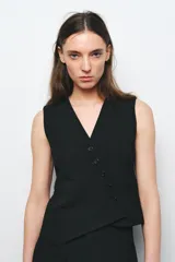 Chaleco negro de Zara Woman Collection, con escote pico y sin mangas. Presenta falsos bolsillos de vivo en el delantero, bajo asimétrico y cierre frontal cruzado con botones.