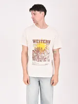 Remera color crudo con estampa frontal de estilo western con texto y paisaje desértico.