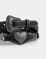 Cinturón negro de cuero sintético con hebilla metálica labrada y apliques de corazones metálicos con diseño floral.
